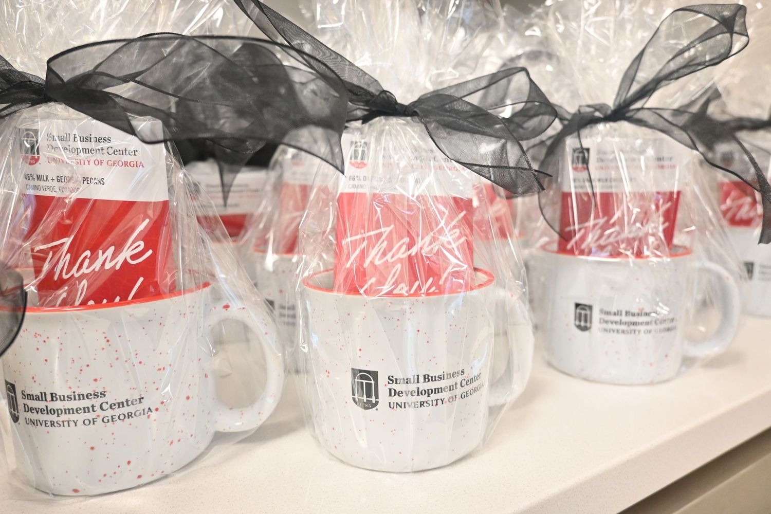 Small Business Development Center University of Georgia branded mugs wrapped with black ribbon bows and thank you cards on display.