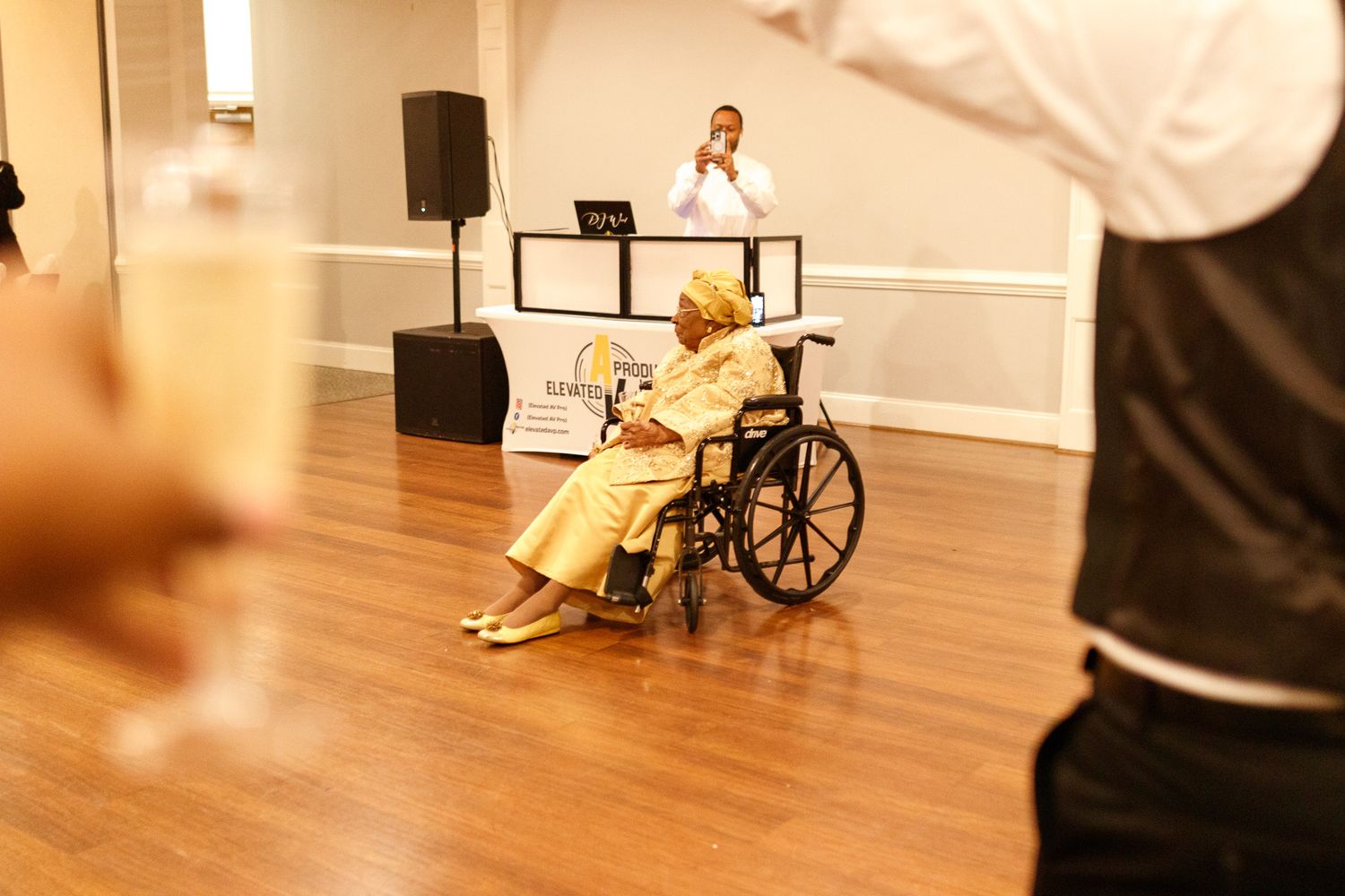 Someone in a yellow dress sits in a wheelchair at what appears to be a dance or event venue.