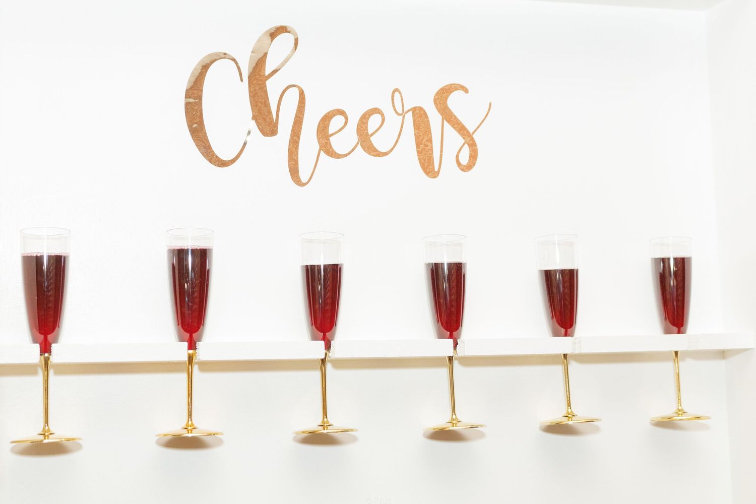 Row of elegant champagne glasses filled with red wine or cocktails against a white background set for a celebration.