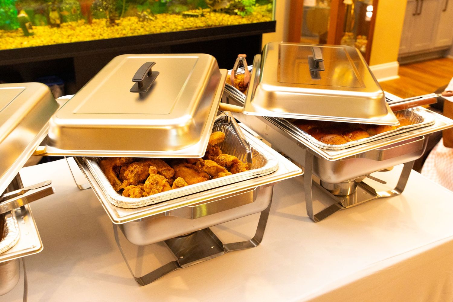 Row of stainless steel chafing dishes set up for catering service under warm lighting.