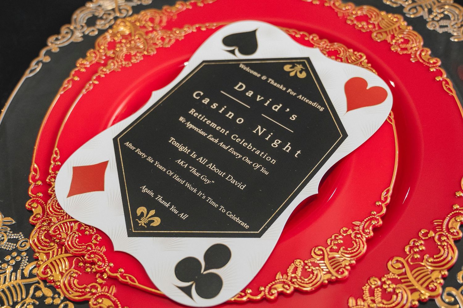 Elegant black hexagonal playing card themed invitations with gold trim displayed on red and gold backgrounds.