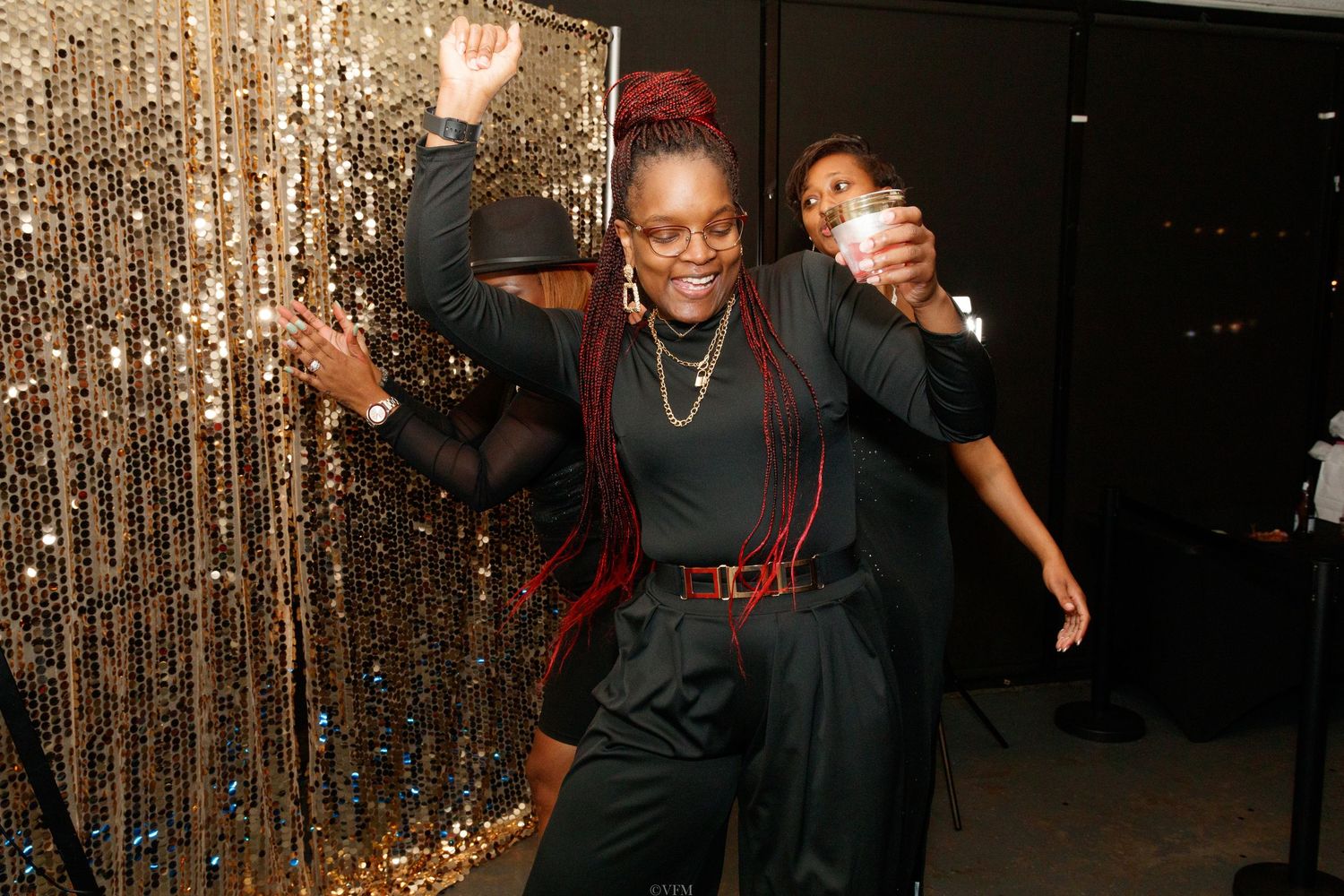 People dancing and enjoying themselves at a party with a glittering gold curtain backdrop.