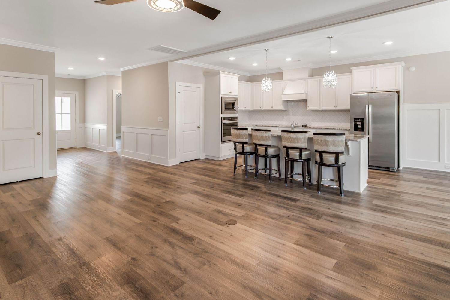 Open-concept kitchen with white cabinets, stainless steel appliances, island seating, and hardwood floors.