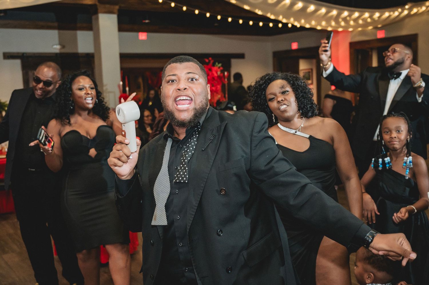 People in formal attire dancing and enjoying themselves at an indoor party with string lights.