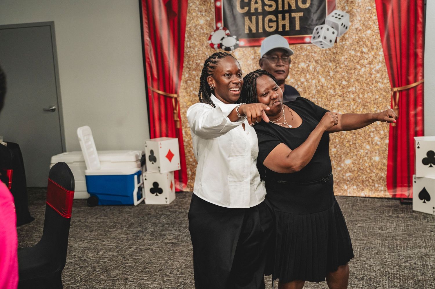 Partygoers enjoying themselves at a casino night celebration with sparkly gold backdrop and red curtains.