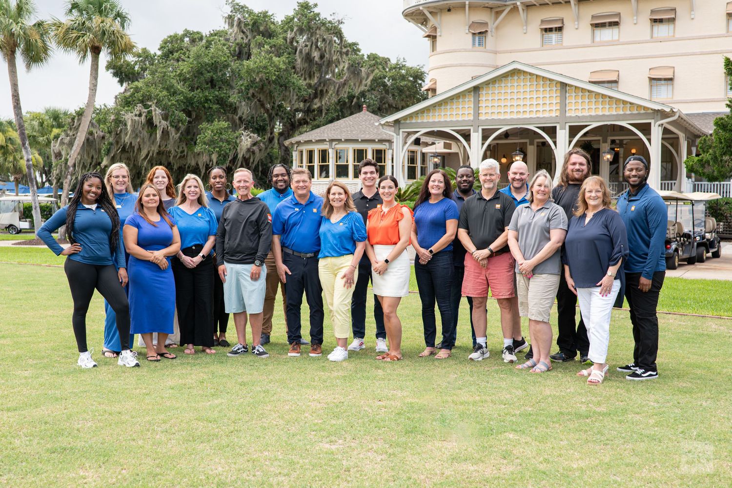 Group of professionals posing outdoors on a golf course lawn near a clubhouse on a sunny day.
