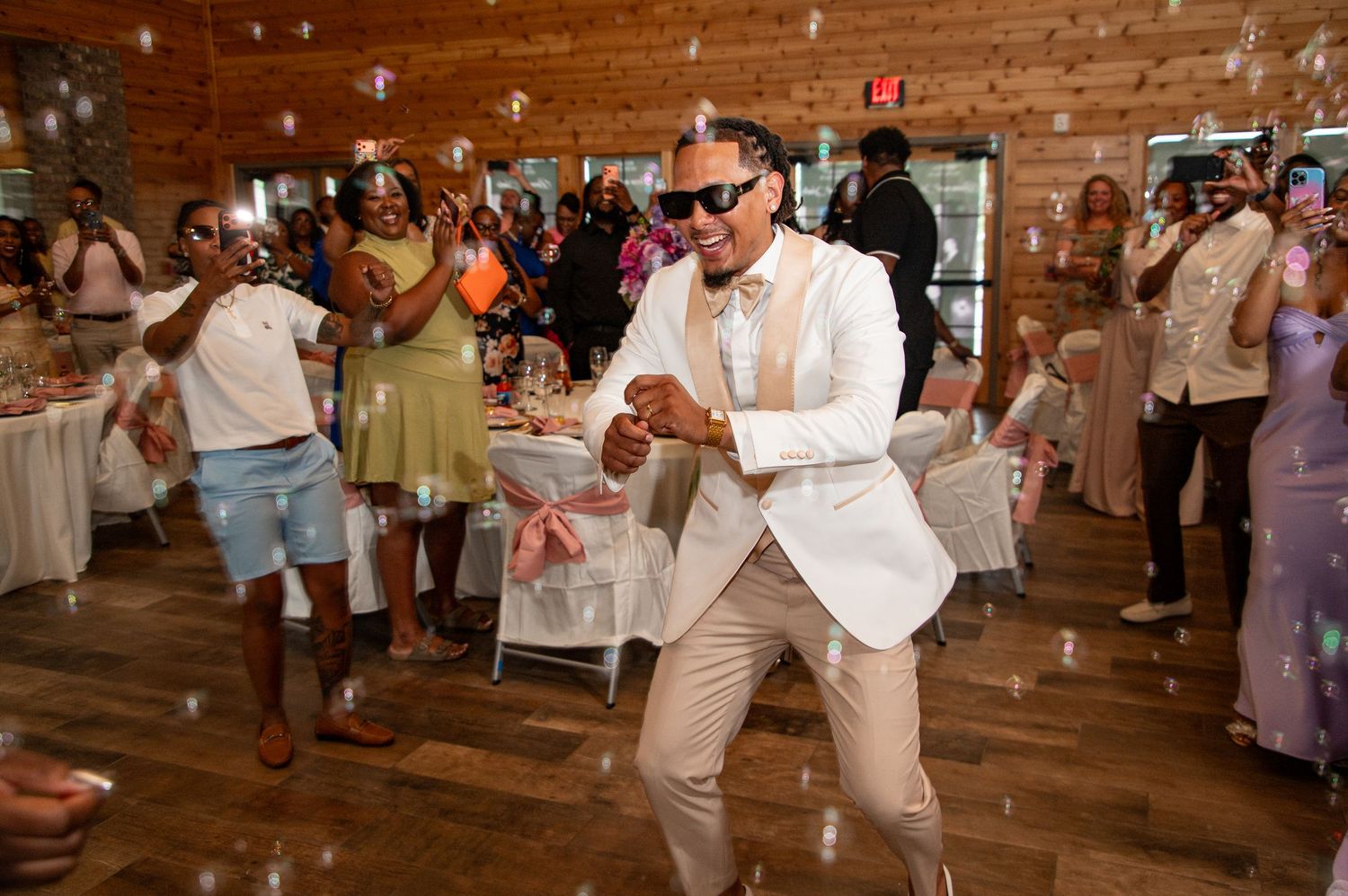 Groom in white jacket dancing with guests at lively wedding reception.