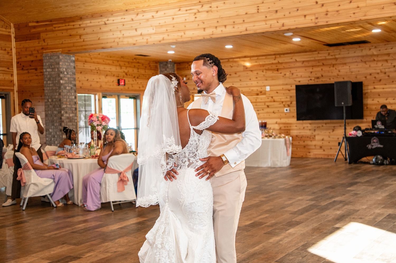 Newlyweds share romantic first dance embrace in sunlit rustic wedding reception hall.