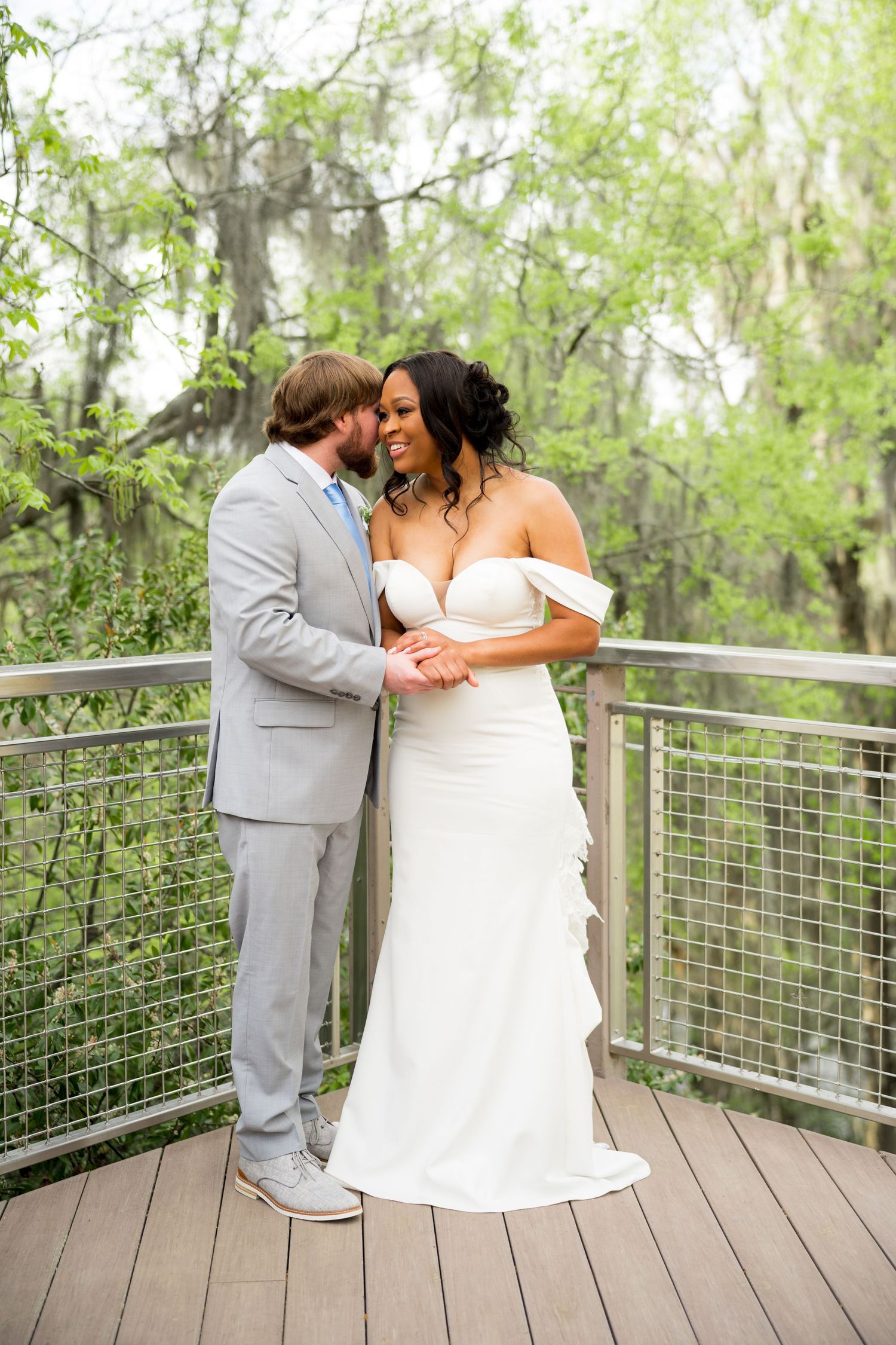 A bride and groom share a tender moment on a wooden deck surrounded by lush greenery on their wedding day.