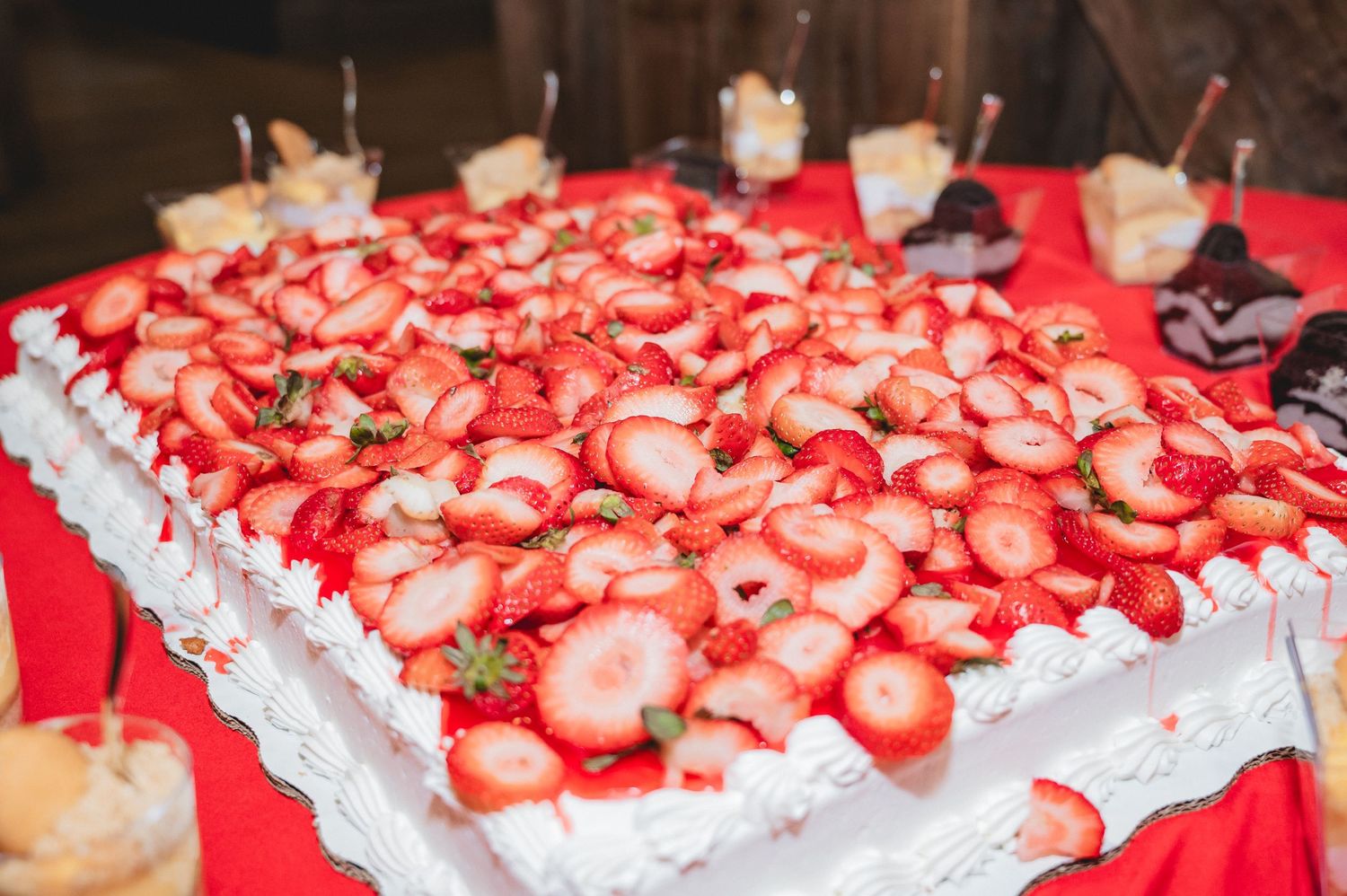 Fresh strawberries garnish a white frosted dessert cake at a festive party with red tablecloth decorations.