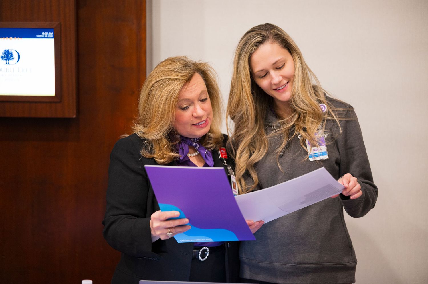 Two professional women reviewing documents together at a business meeting or conference event.