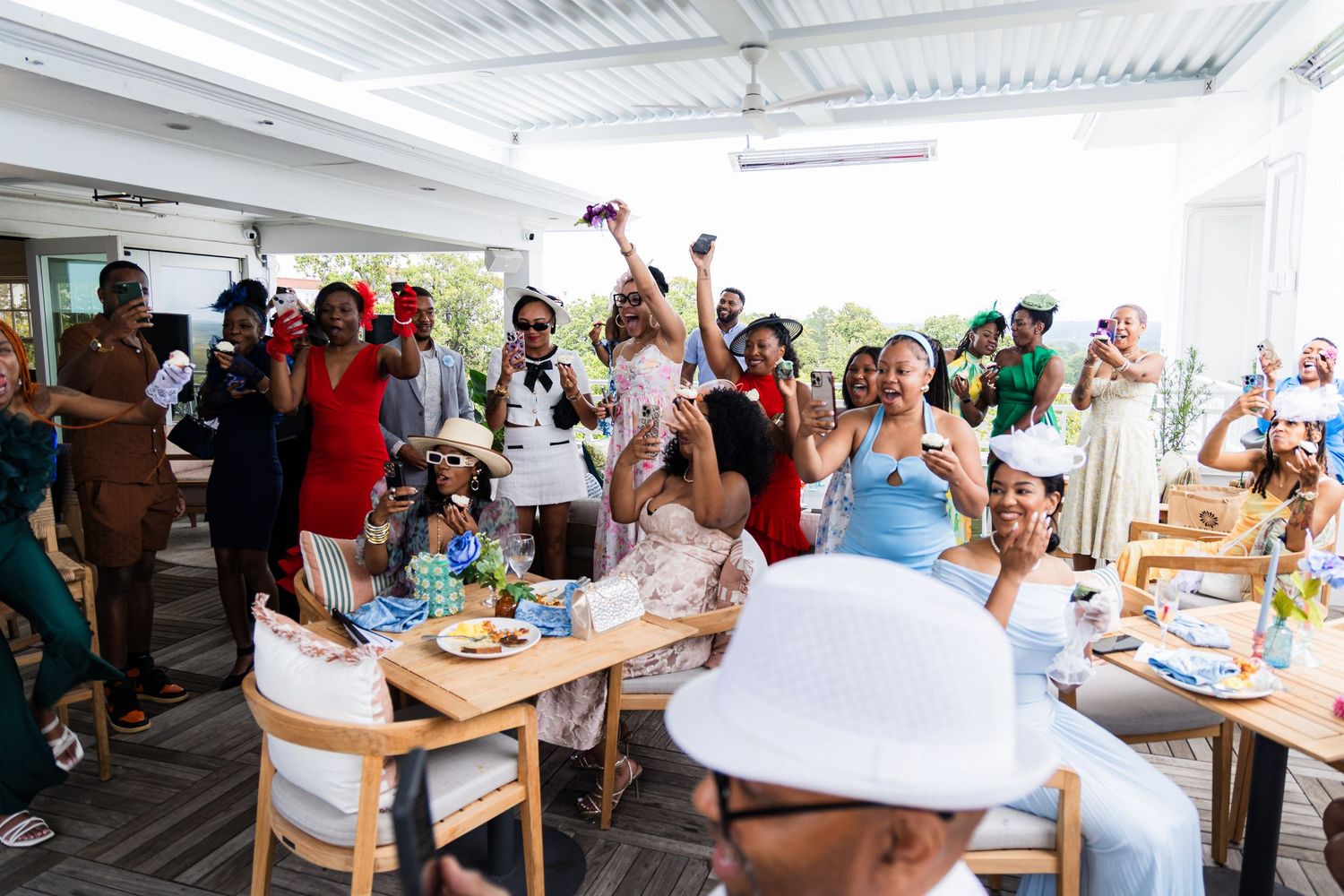 Party guests celebrate and cheer during a joyful gathering in a bright indoor venue with white decor.