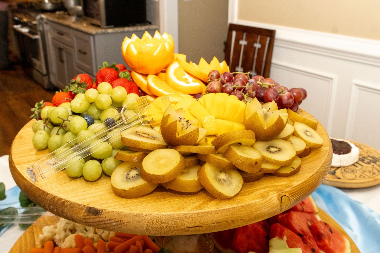 Large wooden platter filled with colorful fresh fruit including grapes, bananas and melons.