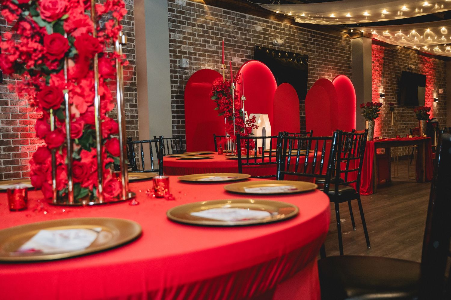 Red decor and string lights create an elegant ambiance in a brick-walled venue space.