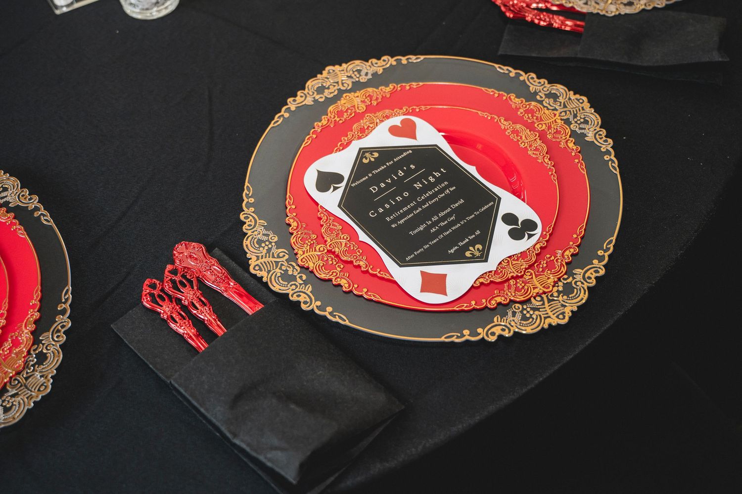 Elegant red and gold place setting with ornate charger plate and matching utensils at a casino-themed event.