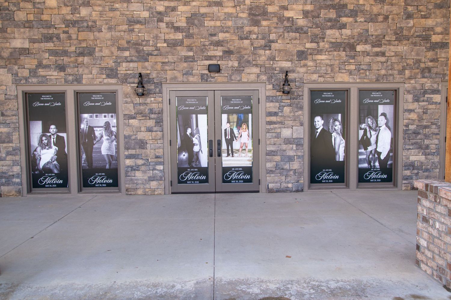 Five elegant venue entrance doors decorated with black and white wedding portrait banners on a brick wall.
