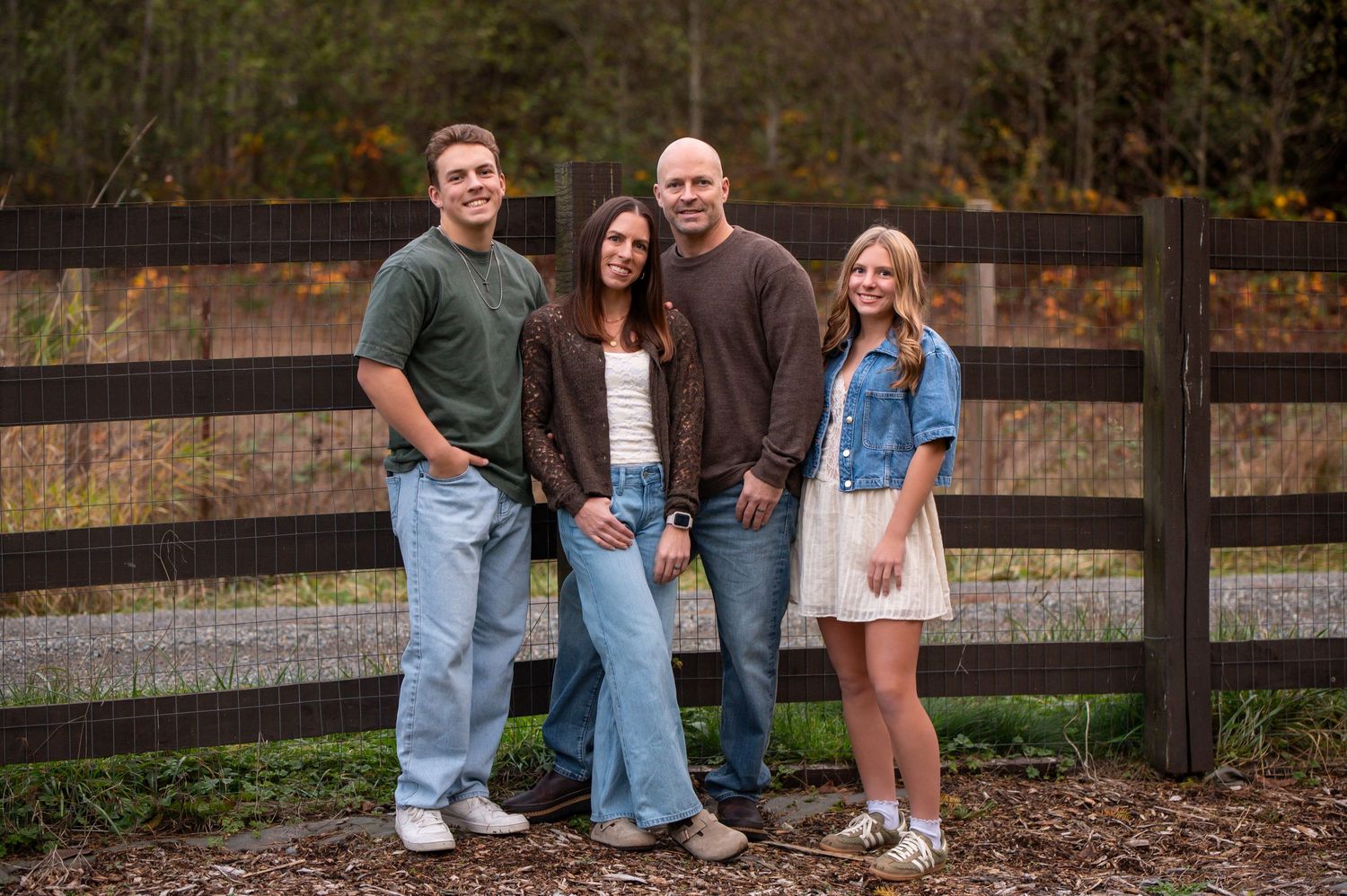 Family photo session with casual outfits against rustic wooden fence in outdoor setting posing for family pictures in Covington, WA