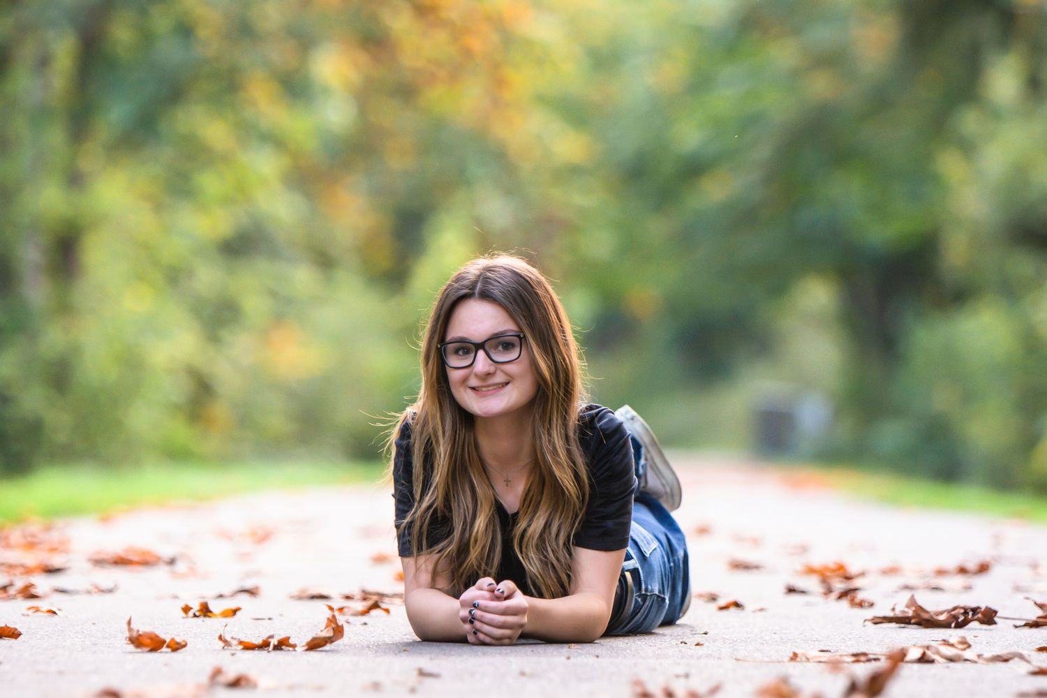 Tahoma Senior wearing glasses lies on autumn leaves with bokeh background during a senior photo session in Maple Valley, WA