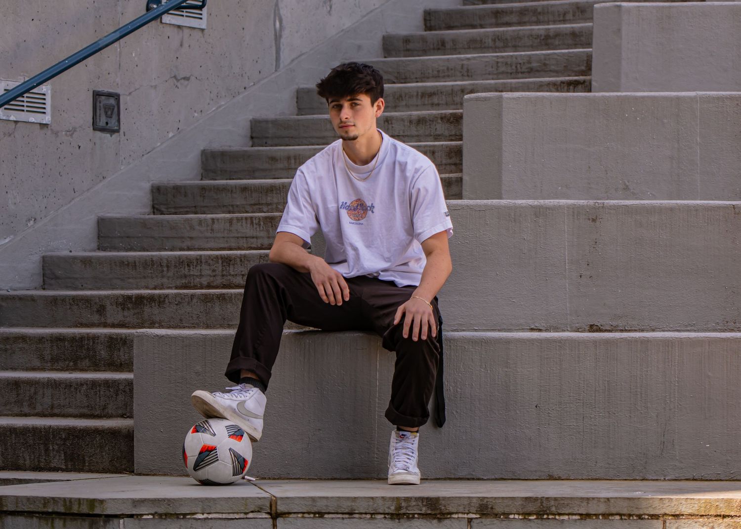 Tahoma Senior practicing soccer ball tricks while sitting on concrete steps during a senior photo shoot in Tacoma, WA
