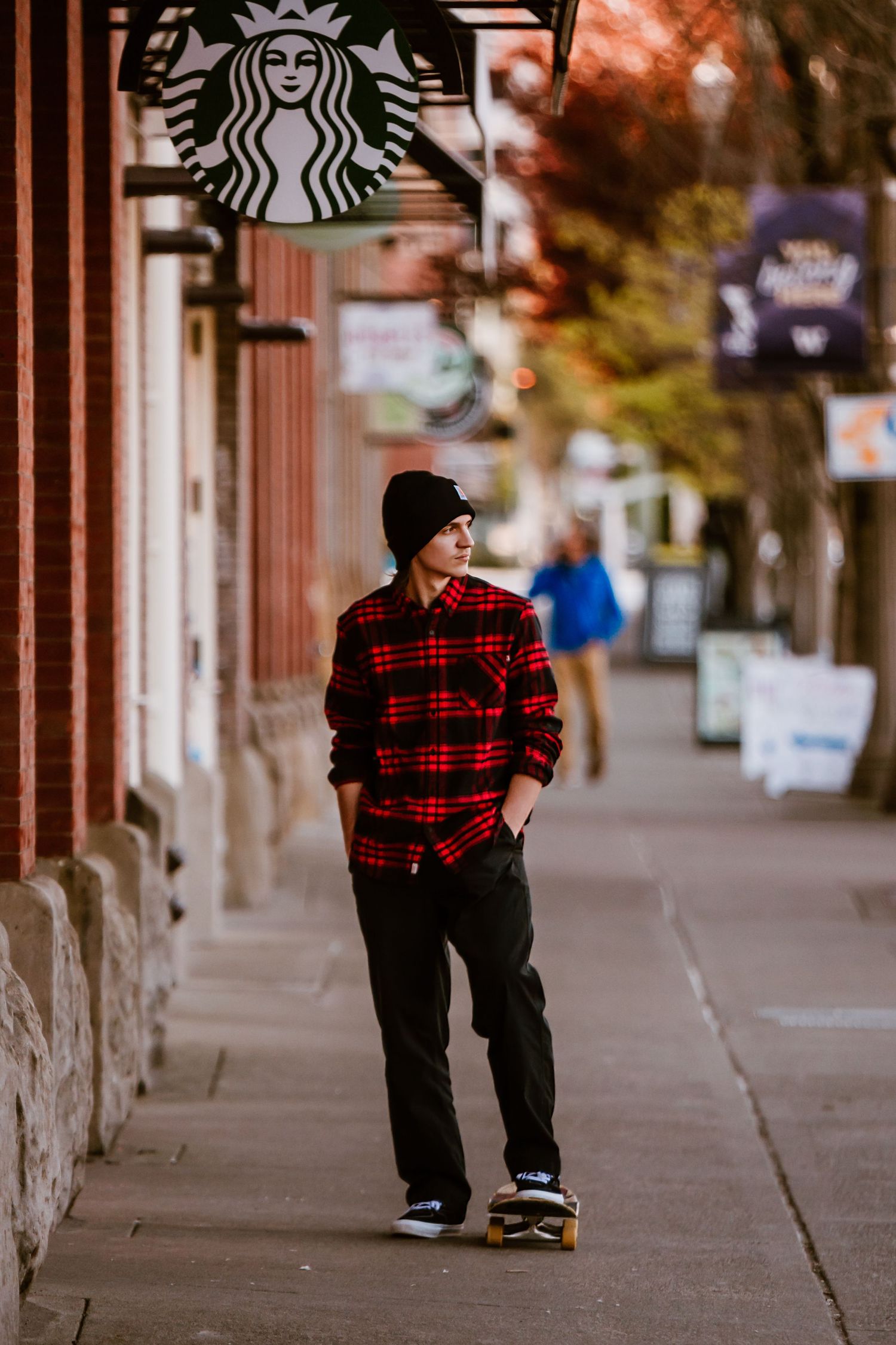 Person skateboarding past Starbucks wearing red plaid shirt and black beanie.