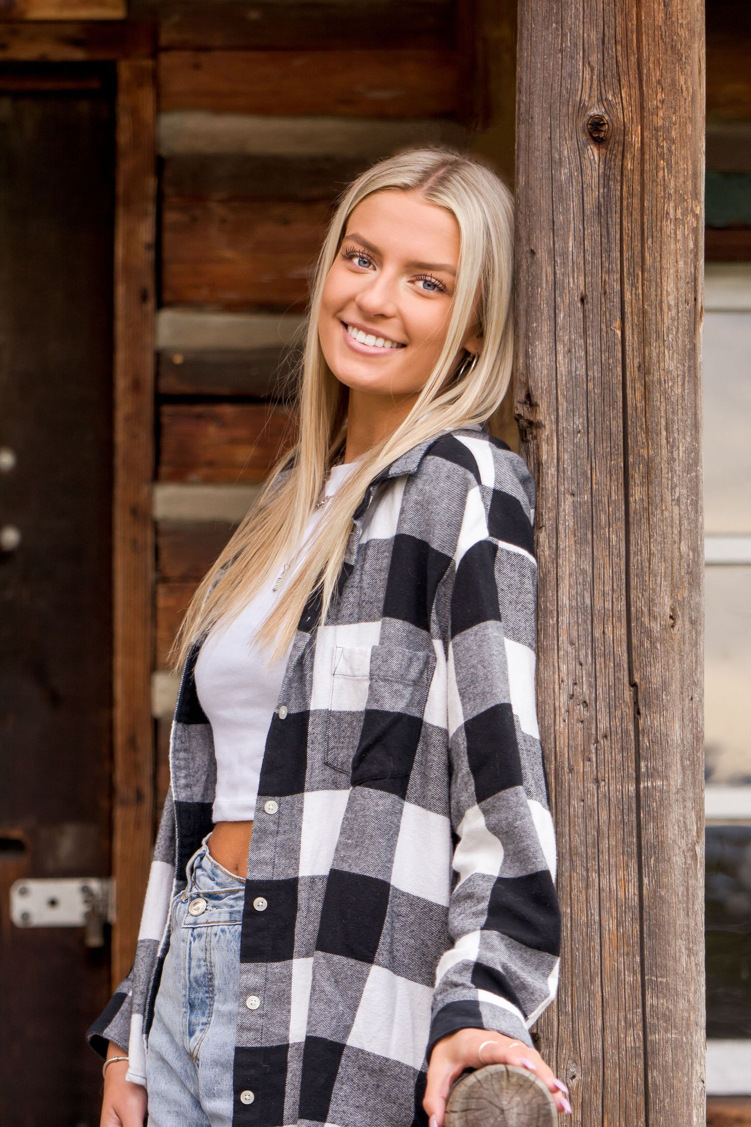 Tahoma Senior in plaid flannel and jeans poses against rustic wooden beams during a senior session in Buckley, WA