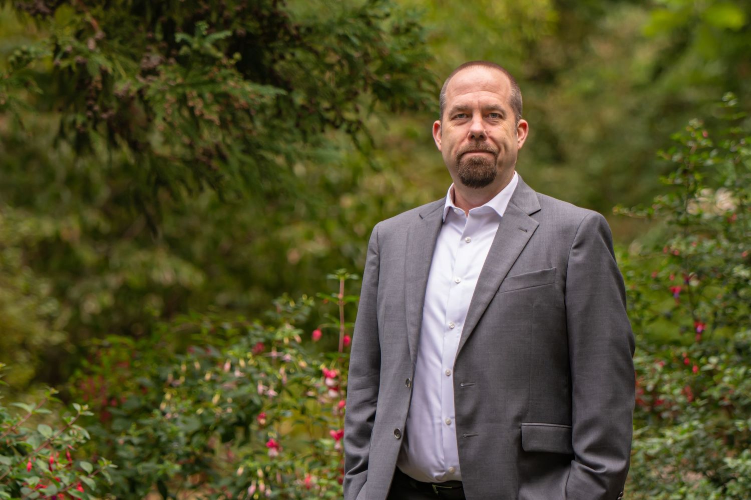 Professional headshots in grey suit against natural garden background poses for a headshot session in Maple Valley, WA