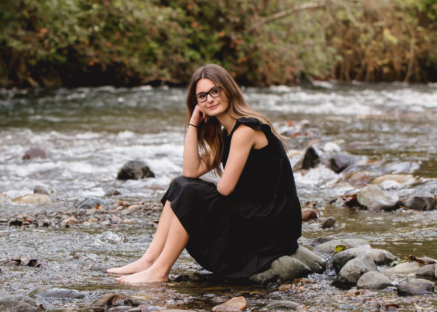 Tahoma Senior in black dress poses near rocky riverbed with flowing water during senior session in Maple Valley, WA