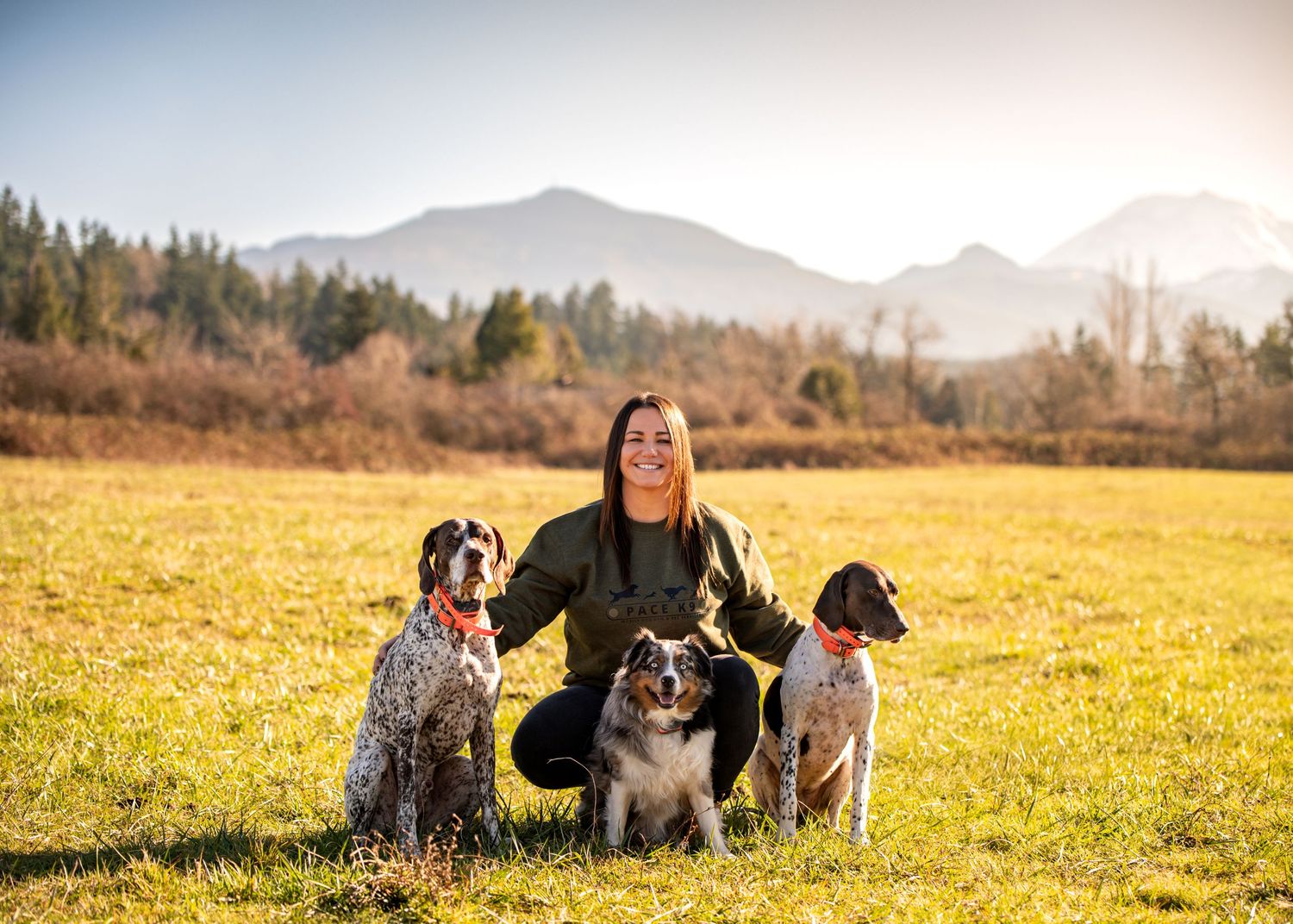 Person with three dogs posing in meadow with mountain landscape in background for a branding session in Enumclaw, WA