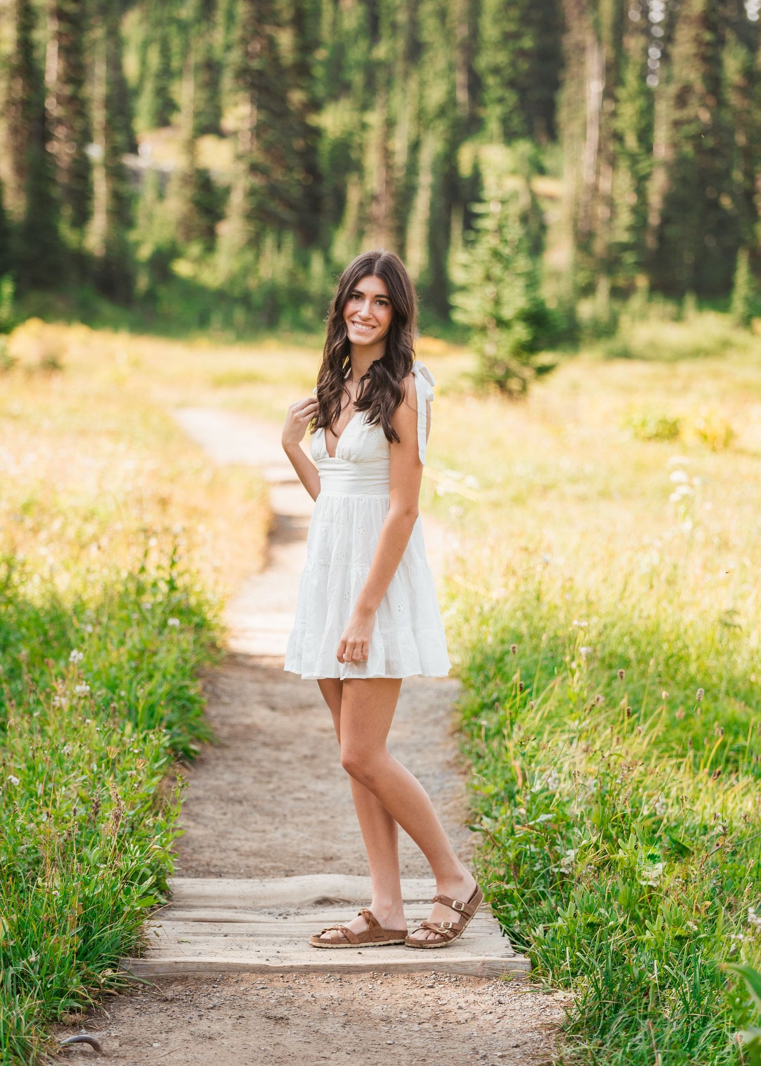 Outdoor portrait senior session on dirt path surrounded by mountain wildflowers and pine trees on Mount Rainier