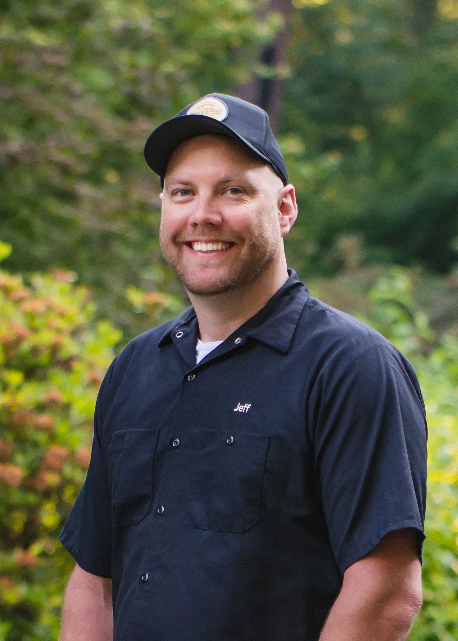 Man in black polo and baseball cap poses in natural outdoor setting during a corporate Headshot session in Maple Valley, WA