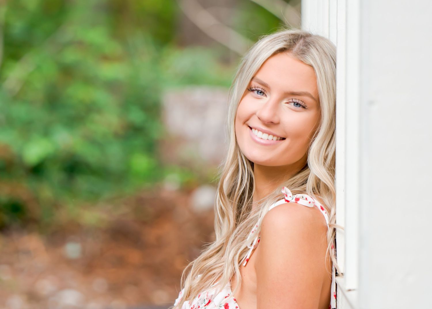 Tahoma HS senior in floral dress poses against white column with natural background during a senior photo shoot in Ravensdale, WA