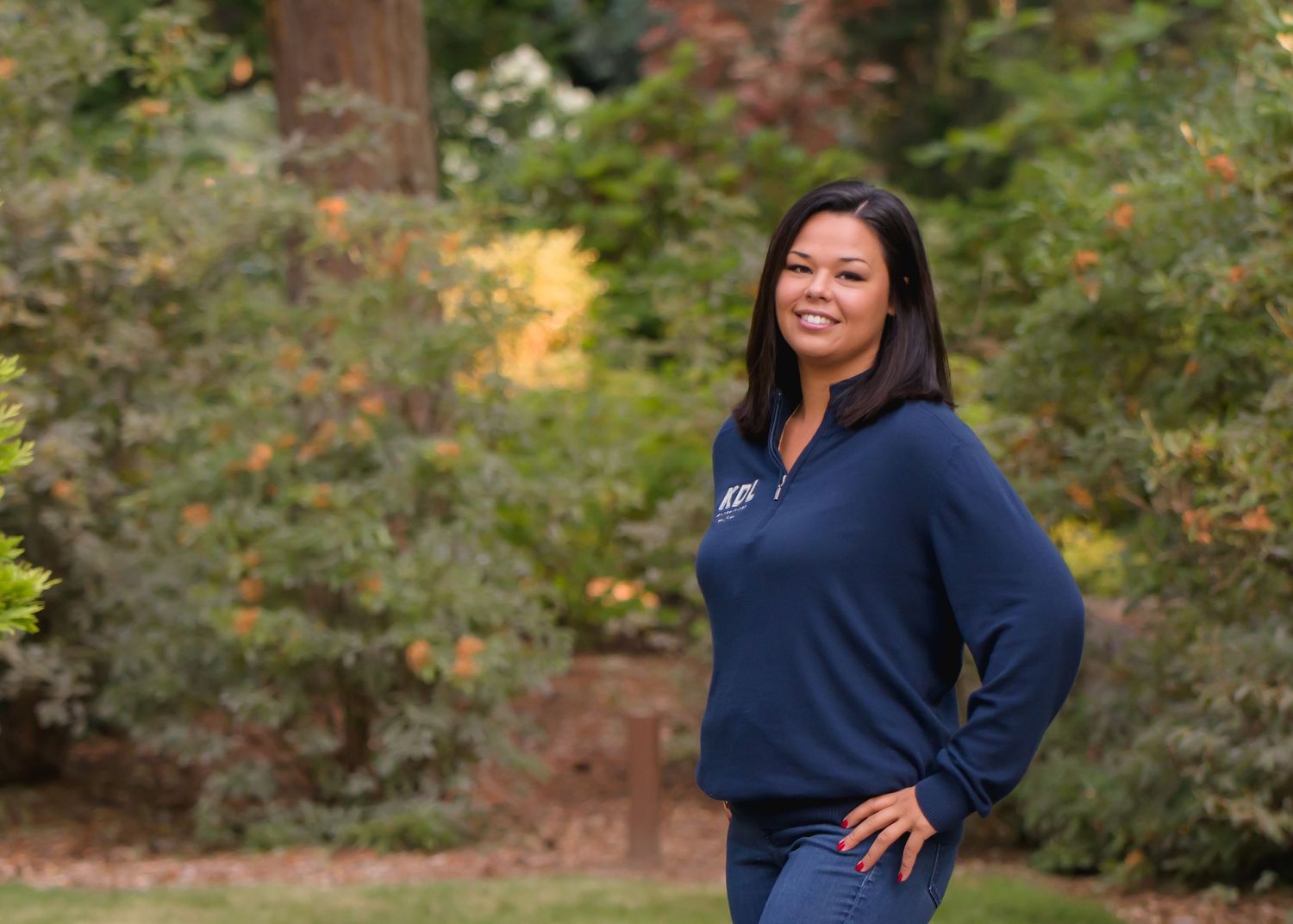 Woman in navy blue sweater poses outdoors with autumn foliage in background during a corporate Headshot session in Maple Valley, WA