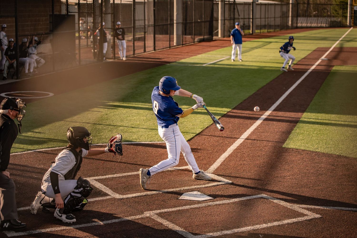 Baseball batter prepares to swing at home plate during evening game while catcher crouches behind plate.