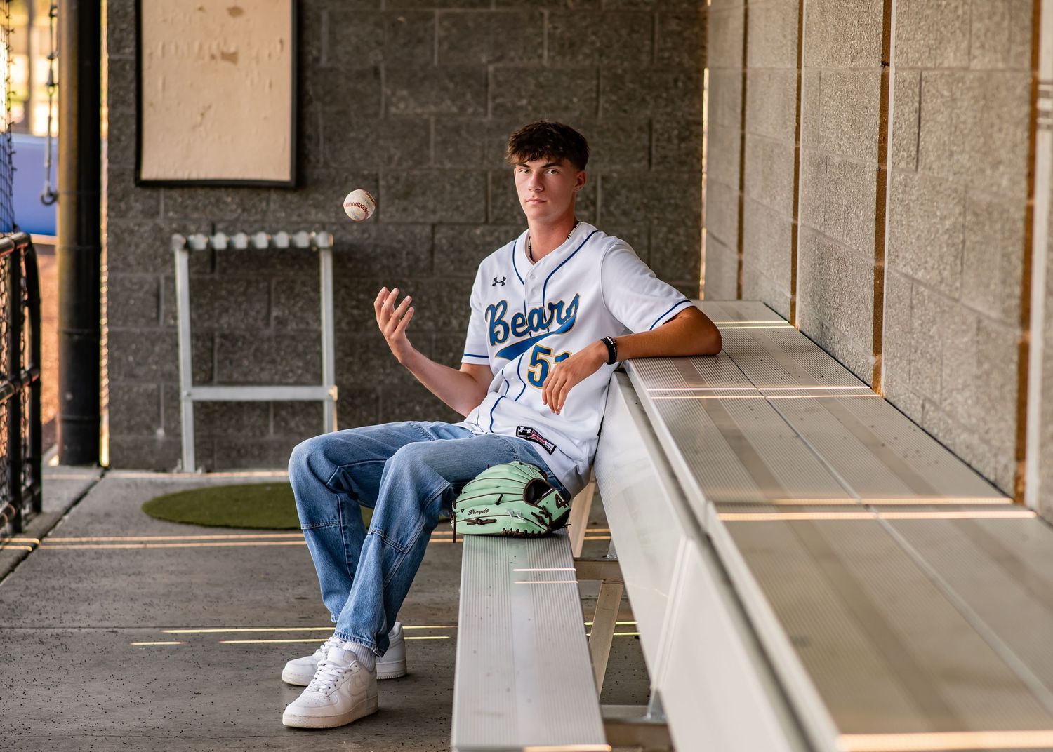 Tahoma baseball player posing in jersey on the bench in the dugout during senior photos in Maple Valley, WA
