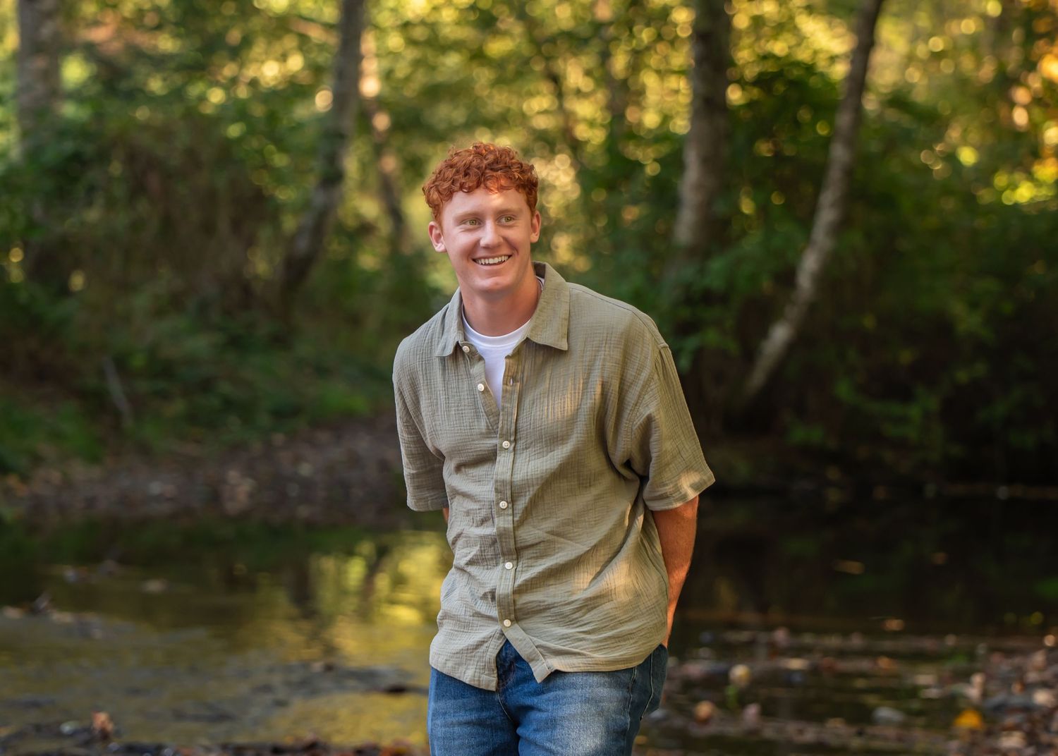 Outdoor senior portrait in wooded setting with golden sunlight filtering through trees. Tahoma HS senior