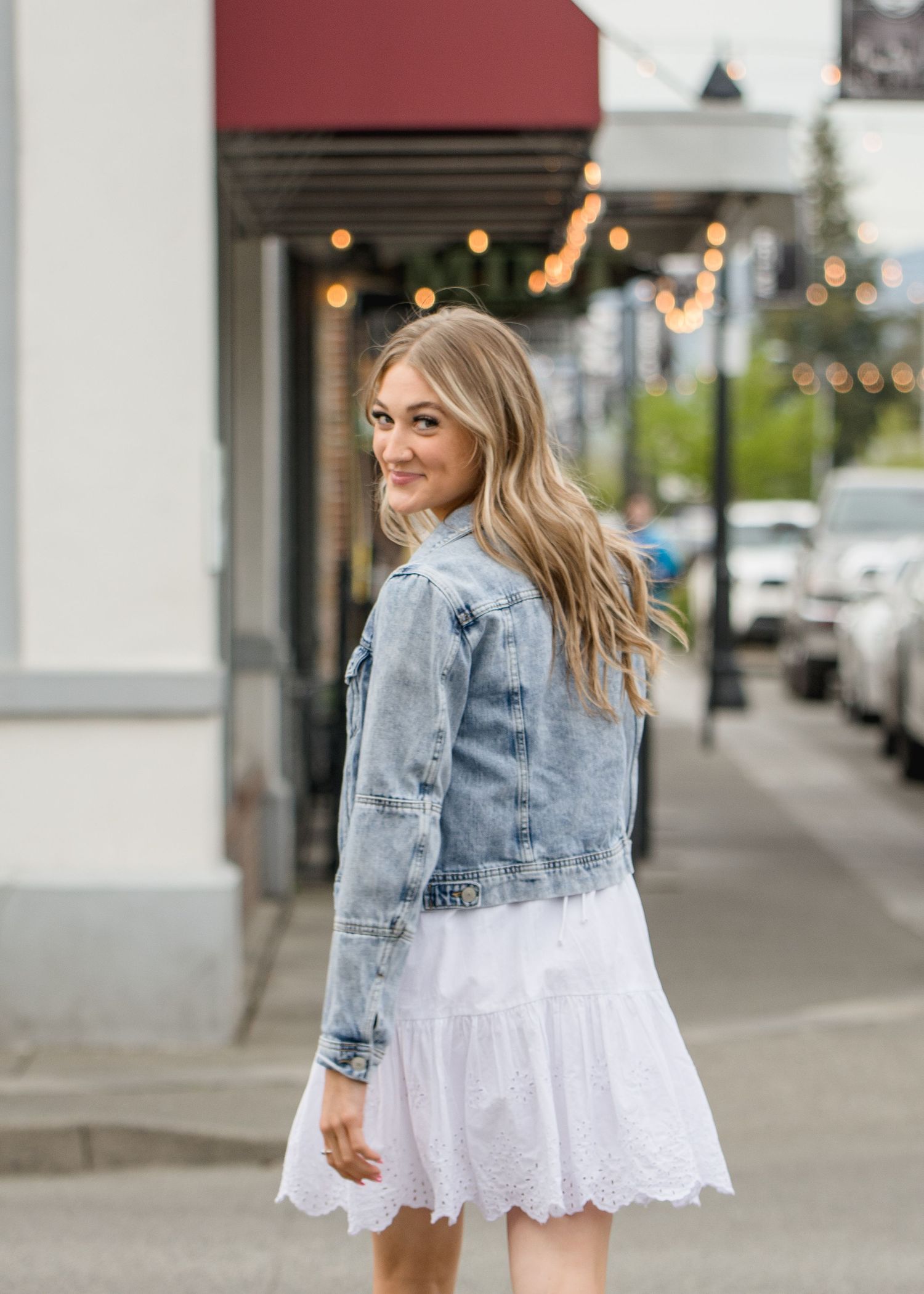 Street style senior shoot with denim and white dress near storefront during senior session in Enumclaw, WA