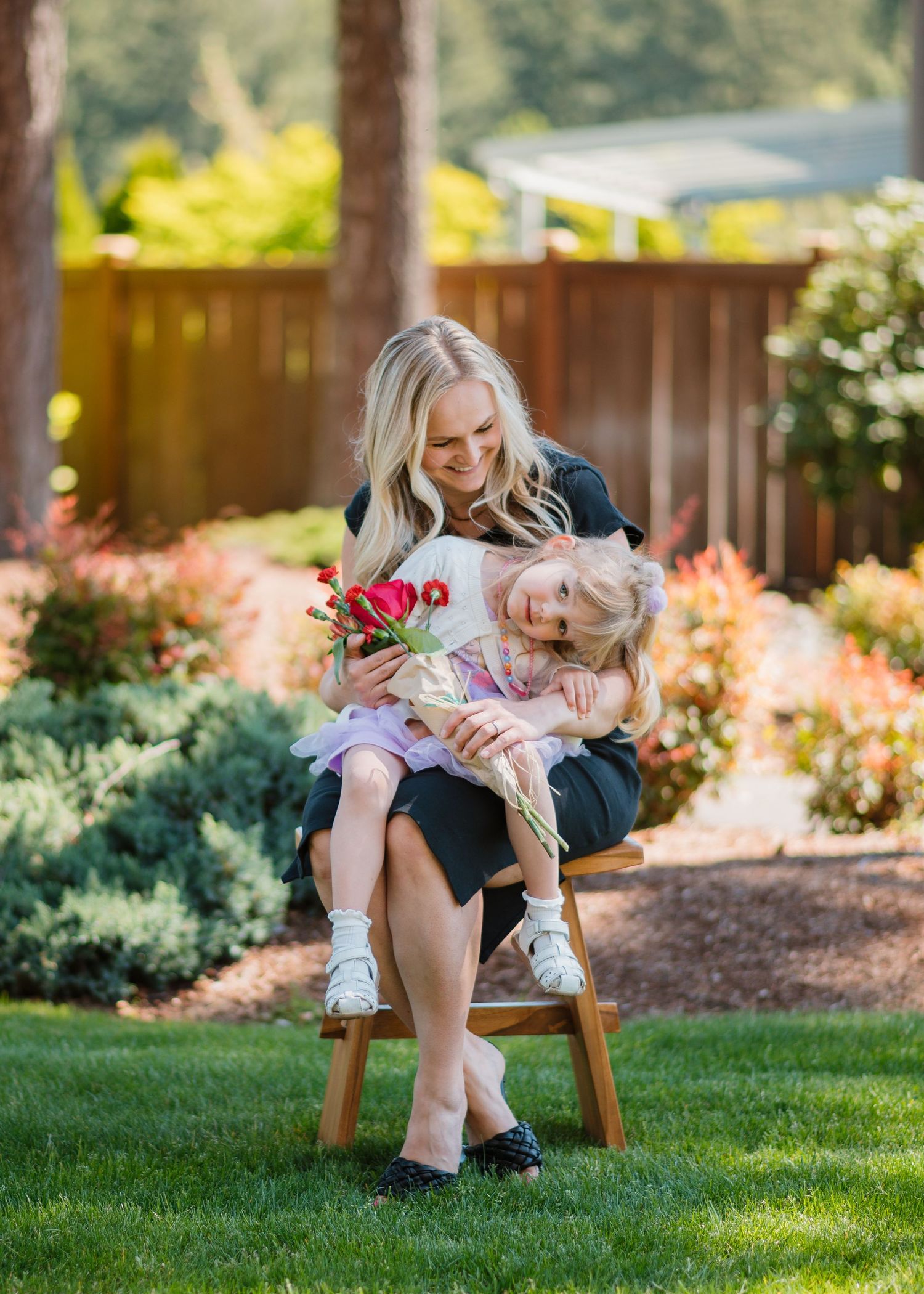 Mother and child embrace while sitting on wooden stool in colorful garden setting for a mother's day mini session in Maple Valley