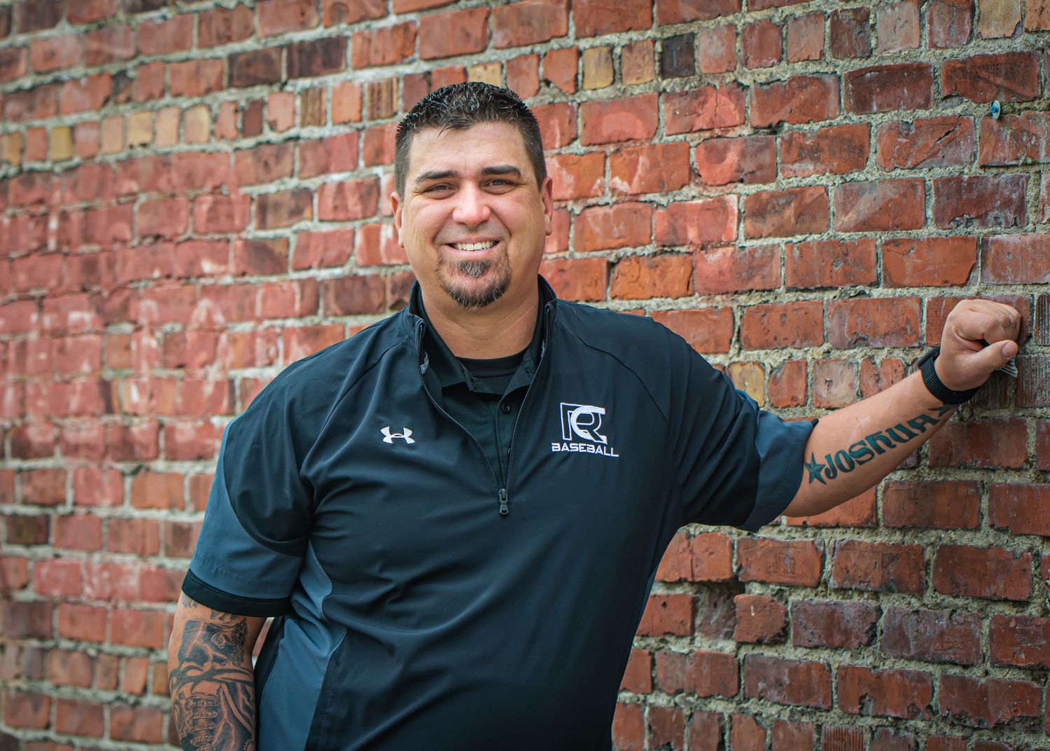 Man in black polo shirt poses playfully against brick wall background for casual headshots in Enumclaw, WA