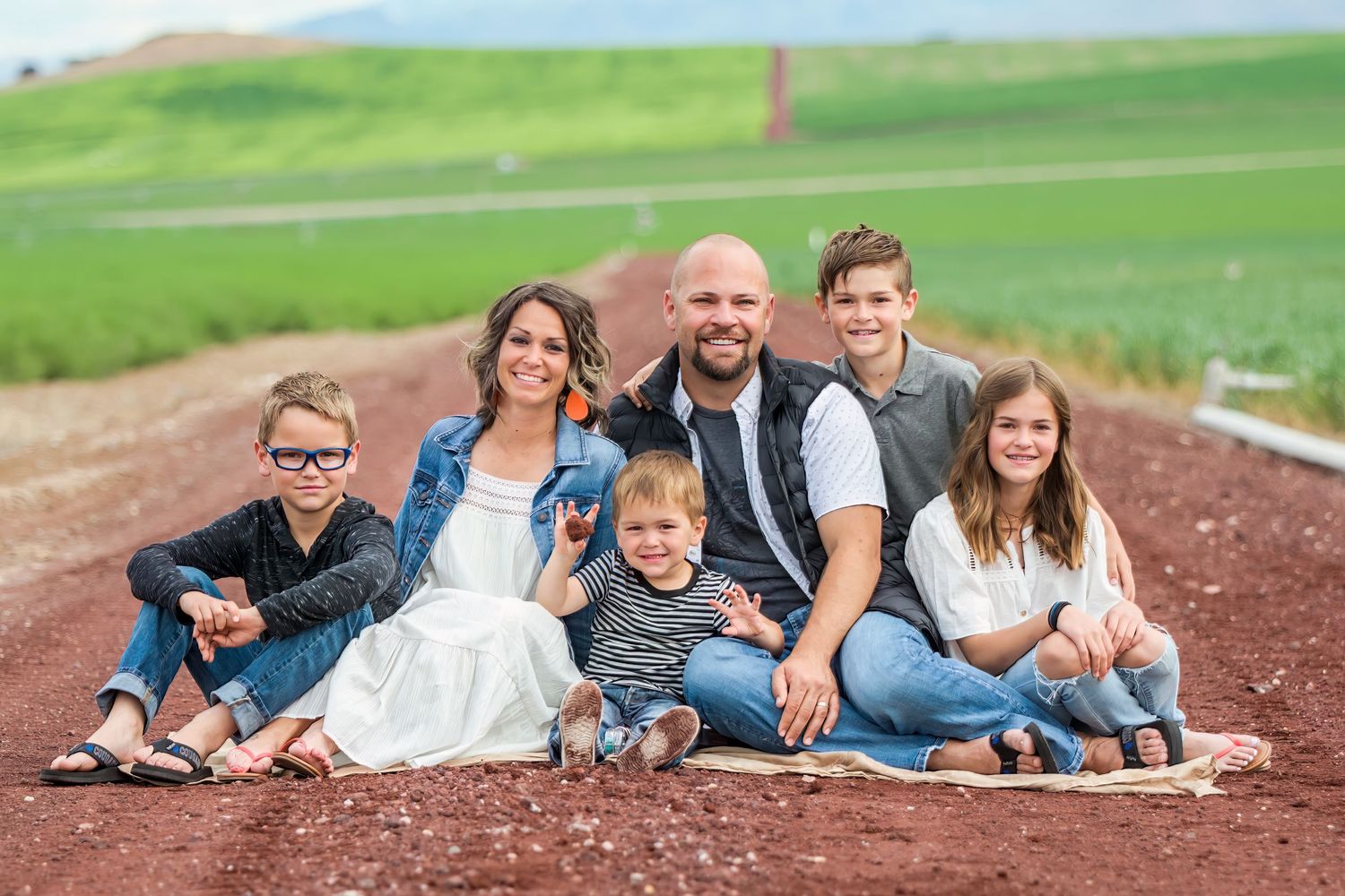 Family lying on brown ground wearing coordinated blue and white outfits during outdoor photo session.