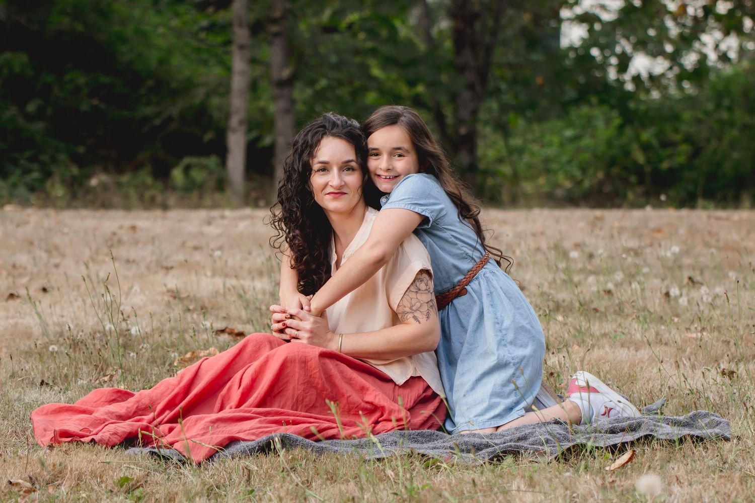 Outdoor photoshoot in a grassy field with mother and daughter sitting on blanket.