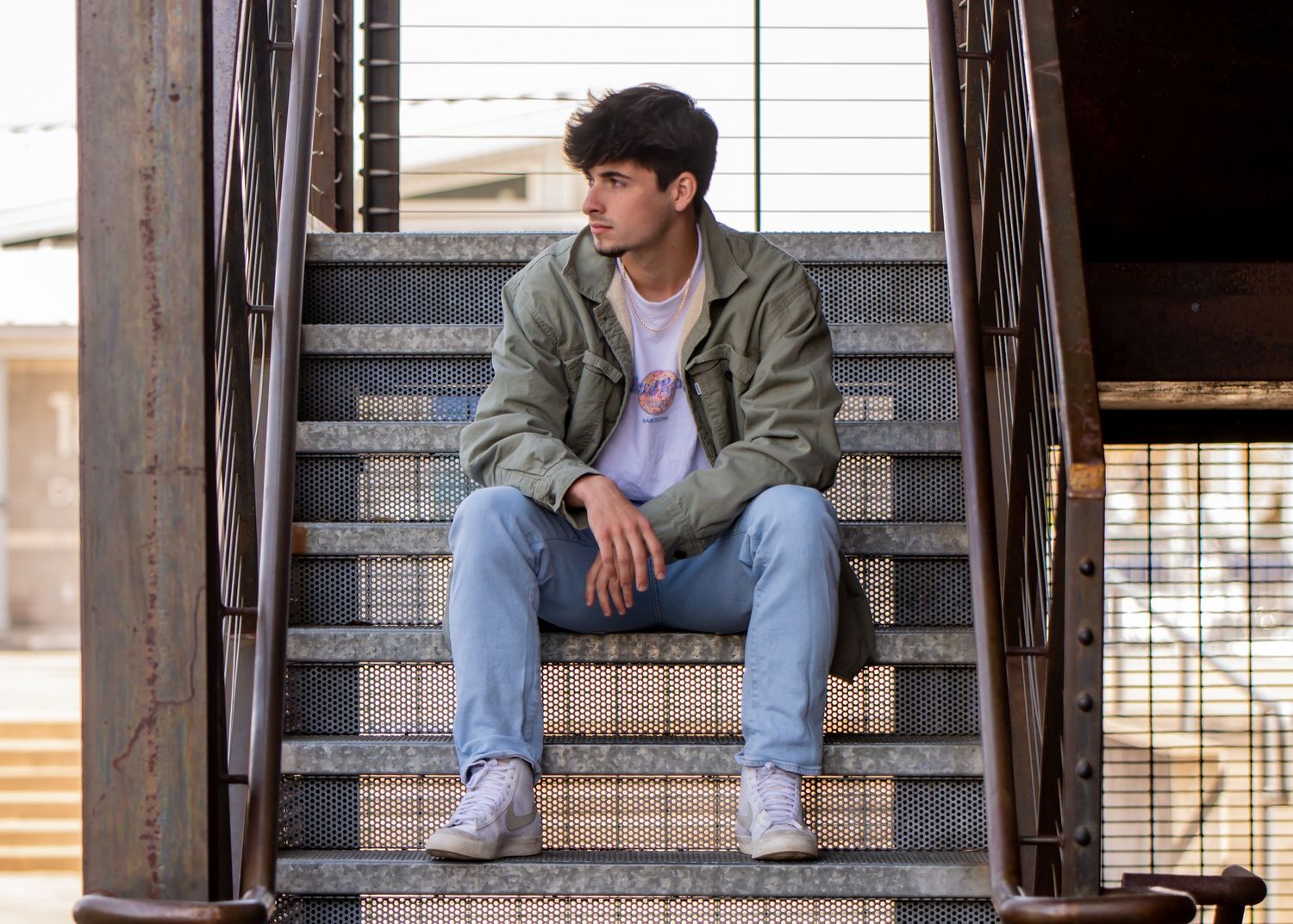 Highschool senior in casual wear sitting on industrial metal stairs during an urban senior photoshoot in Tacoma, WA