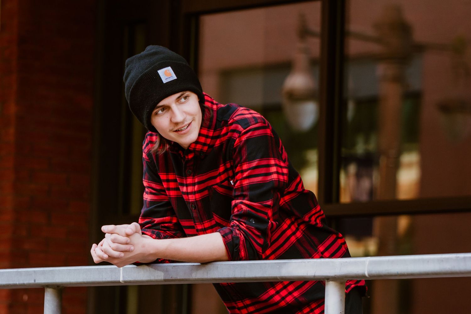Person in buffalo plaid shirt leaning on railing during urban photo session.