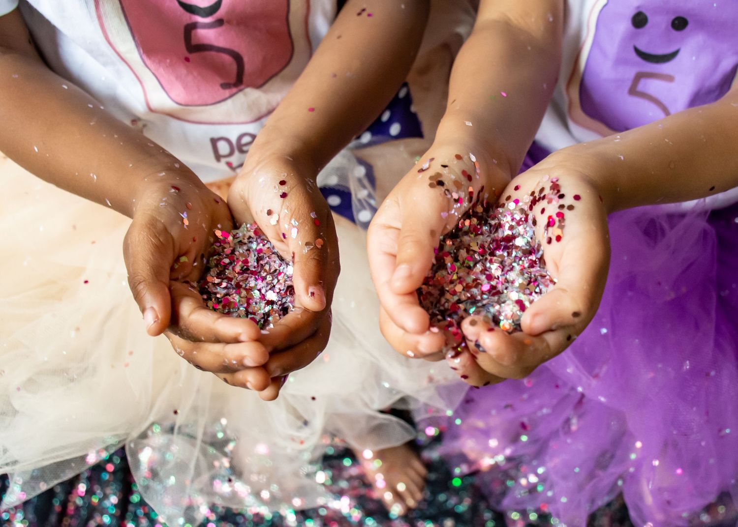 Small hands holding pink and purple glitter with tulle fabric visible in the background.
