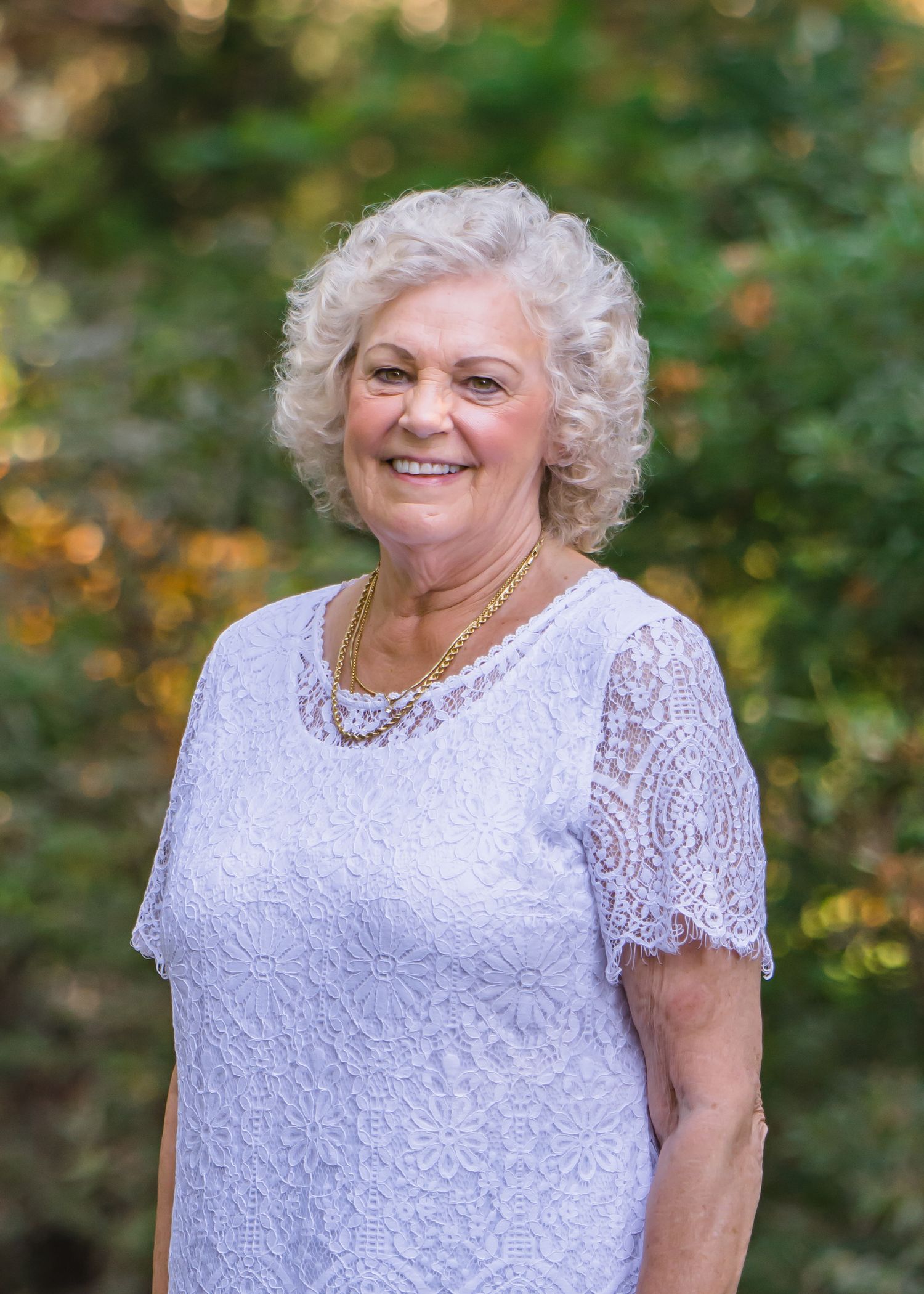 Woman in white lace dress smiles warmly in outdoor garden setting posing during a corporate Headshot session in Maple Valley, WA