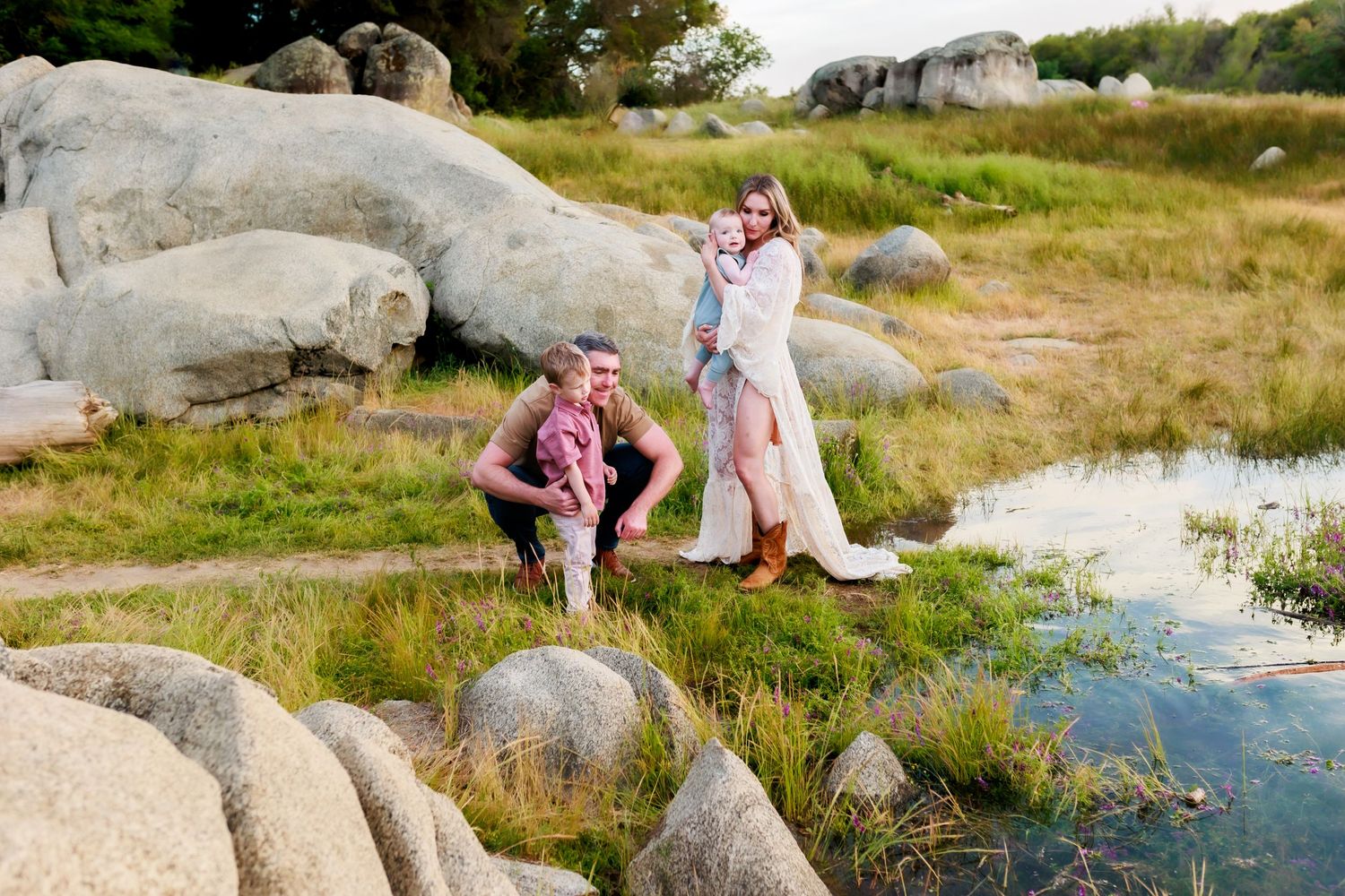 Casual outdoor portrait session on large coastal rocks near the ocean at sunset.