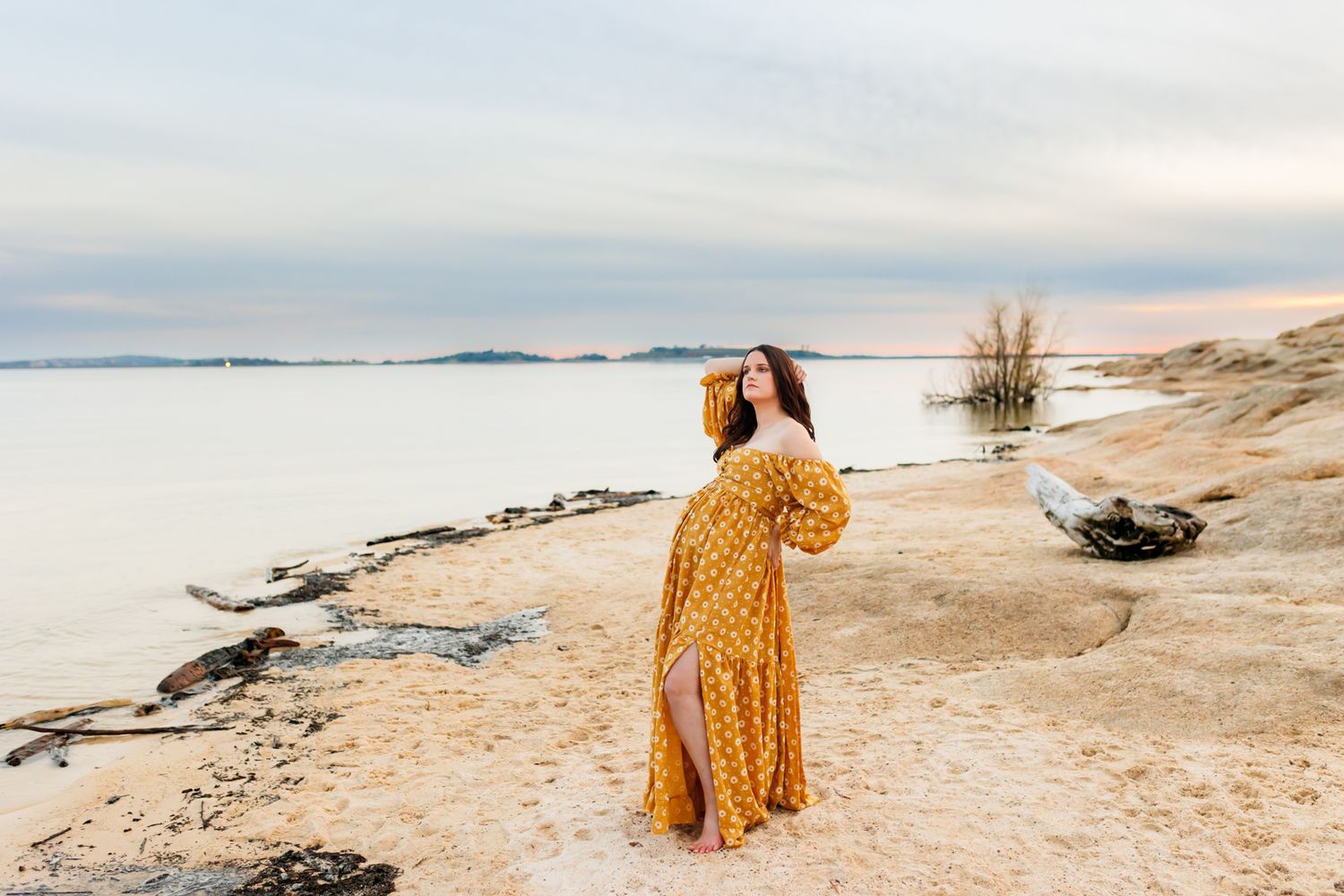 Person in yellow dress walking along scenic beach shoreline at sunset.