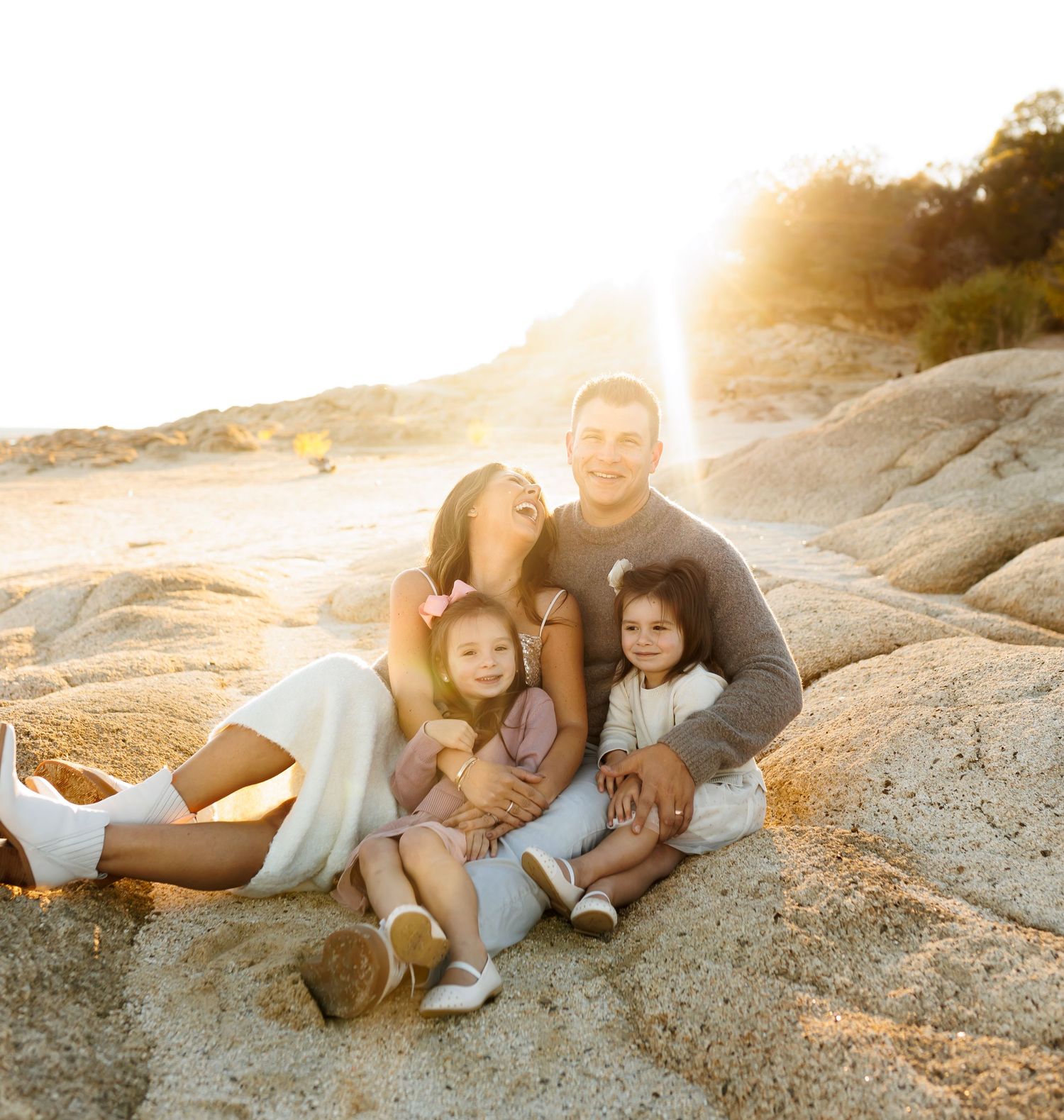 Family relaxing together on rocky coastal terrain during sunset with soft golden lighting.