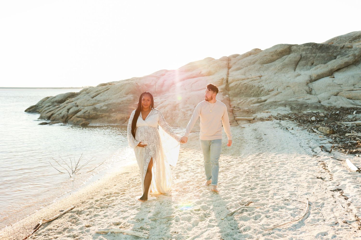 A couple walks along a rocky beach shoreline at sunset with soft dreamy lighting.