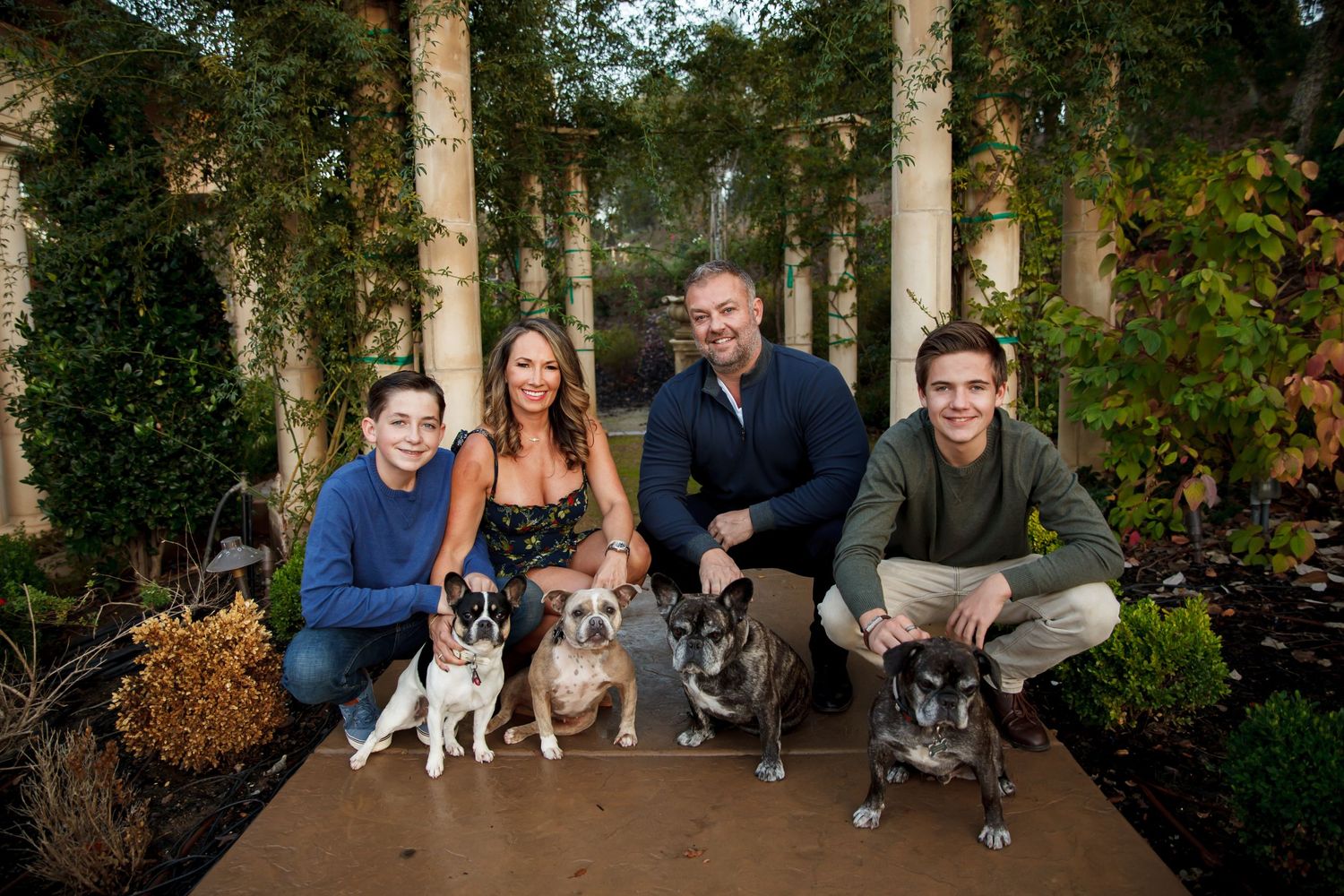 Extended family and pets pose together for a portrait in front of tall columns and greenery.