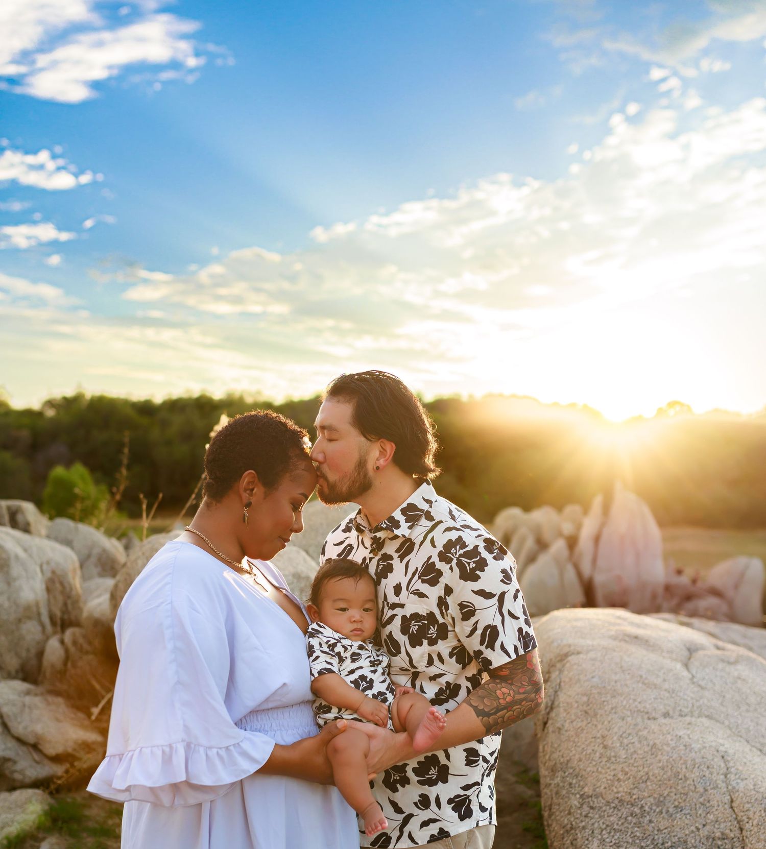 Family shares tender moments together on rocky outcrop during golden hour sunset.